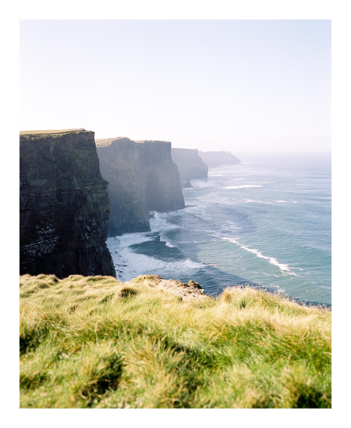 A line of tall, rocky cliffs overlooks a vast ocean with waves crashing against the shore.