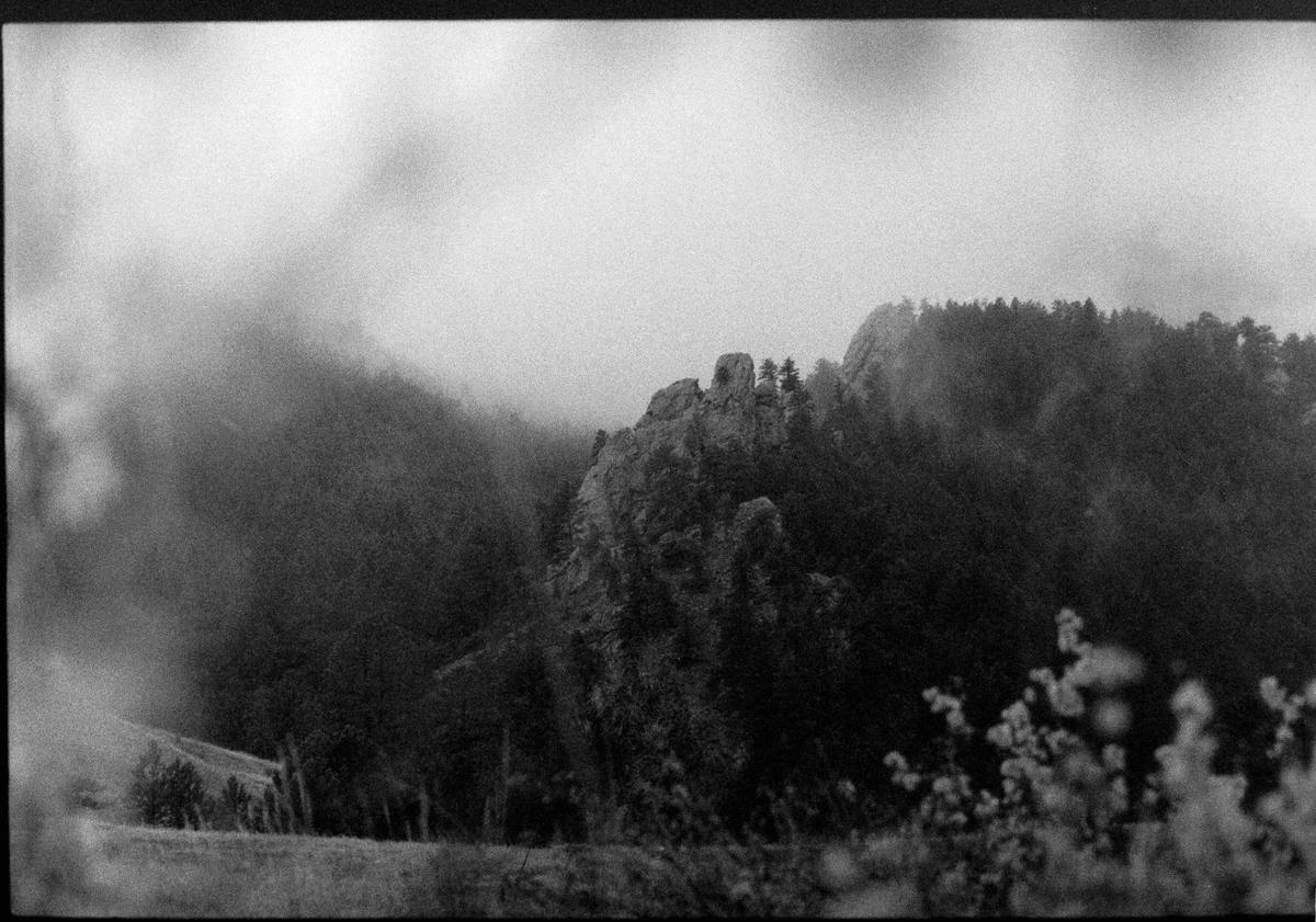 A black and white landscape shows a rocky, forested mountain shrouded in fog.