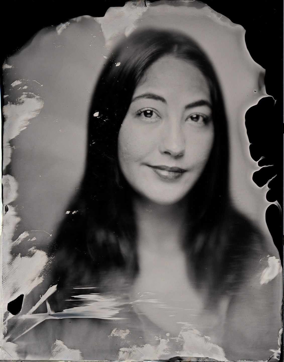 A woman with long hair smiles at the viewer in a black and white portrait.
