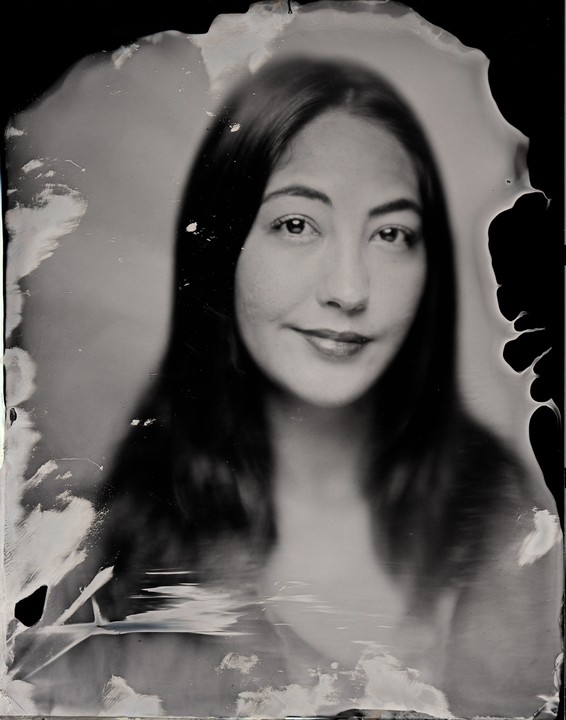 A woman with long hair smiles at the viewer in a black and white portrait.
