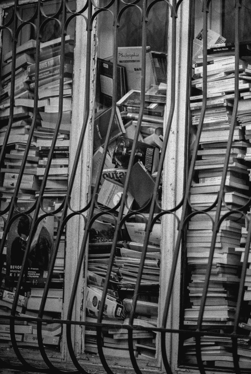 A window is filled with stacks of books behind a decorative metal grate.
