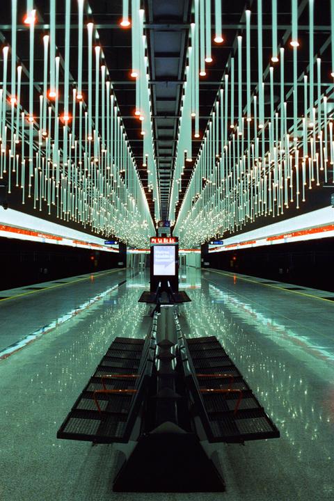 A subway platform is illuminated by numerous hanging lights and reflections on the floor.