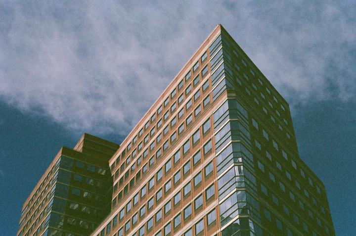 A tall building with many windows is seen from a low angle against a cloudy sky.