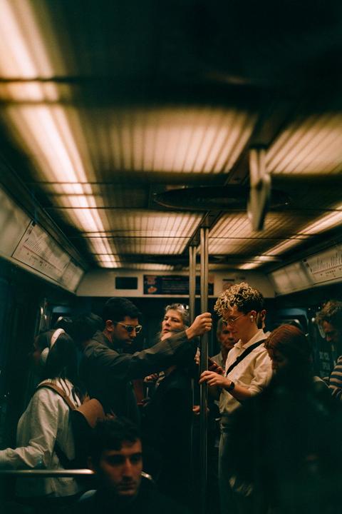A group of people stand in a subway car, some holding onto poles.