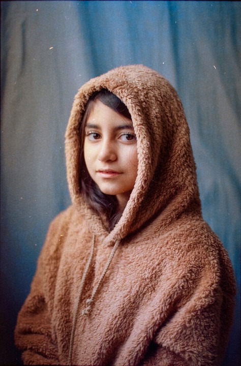 A young woman wearing a fluffy brown hooded sweatshirt looks towards the viewer.