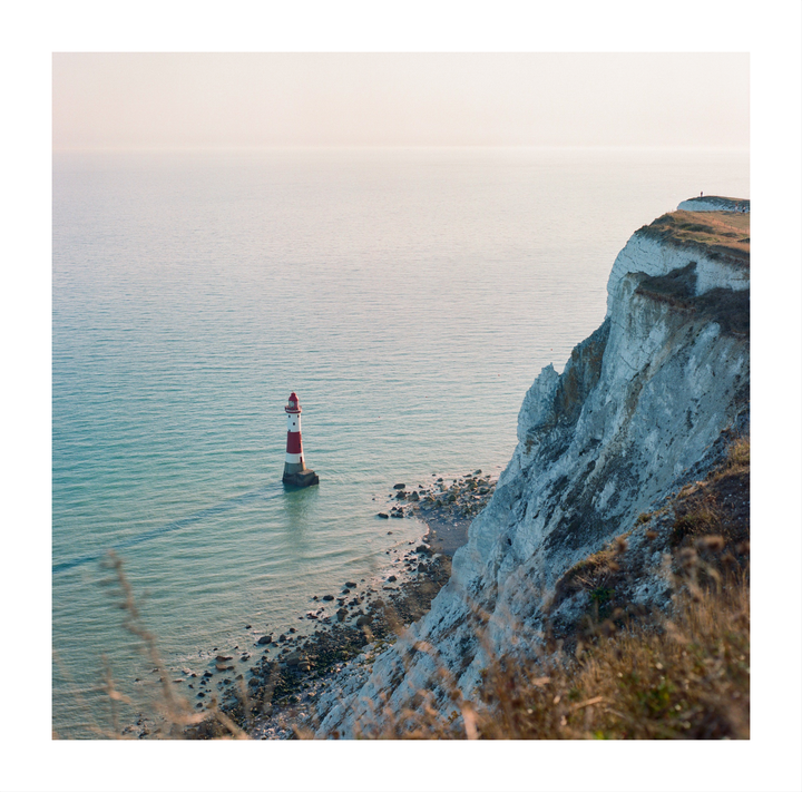 A red and white striped lighthouse stands in the sea next to a white cliff.