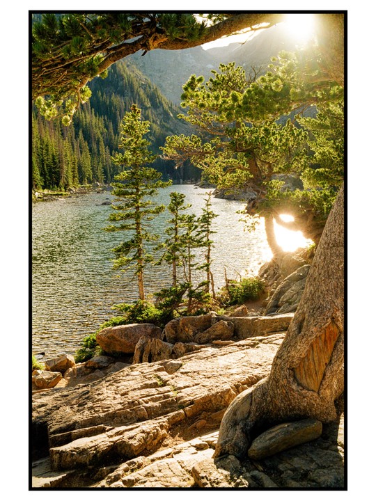 Sunlight shines over a lake surrounded by mountains and pine trees.