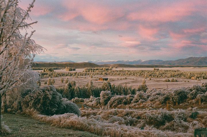 A cabin sits in a vast, frosty landscape under a pink and purple sky.