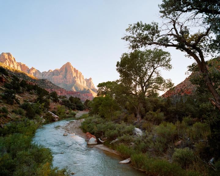 A river flows through a valley with mountains in the background and trees on the banks.