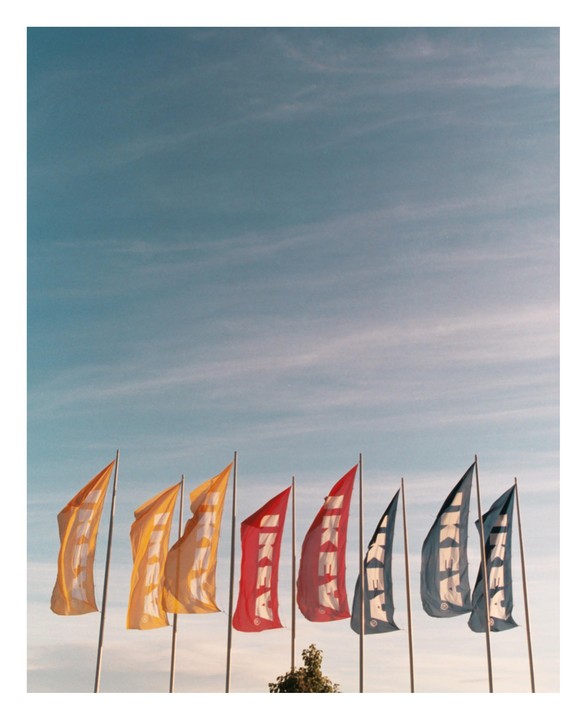 A row of colorful IKEA flags stands against a blue sky with wispy clouds.