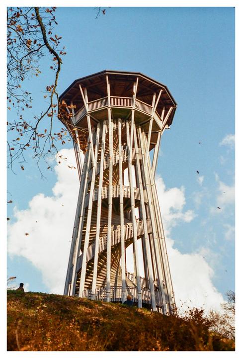 A tall wooden observation tower with a spiral staircase stands against a blue sky with white clouds.