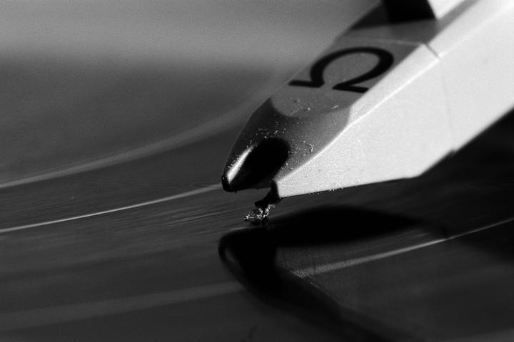A close-up view shows a record player needle covered in dust as it rests on a vinyl record.