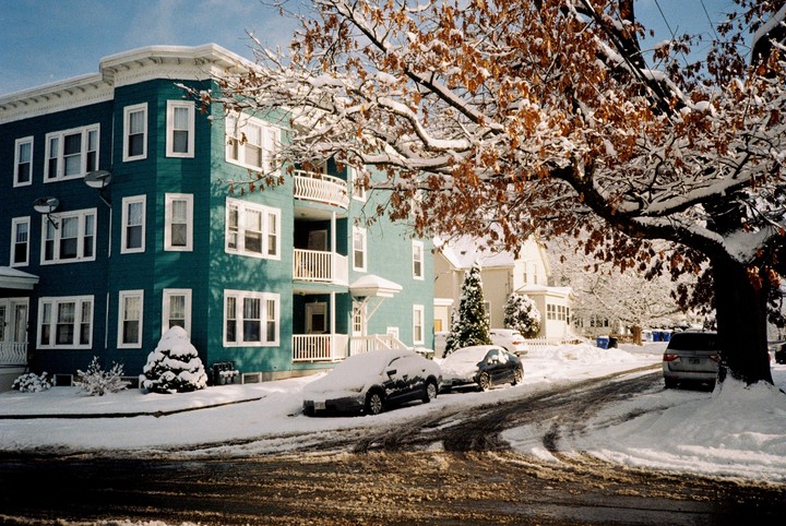 A teal apartment building and cars are covered in snow on a sunny winter day.