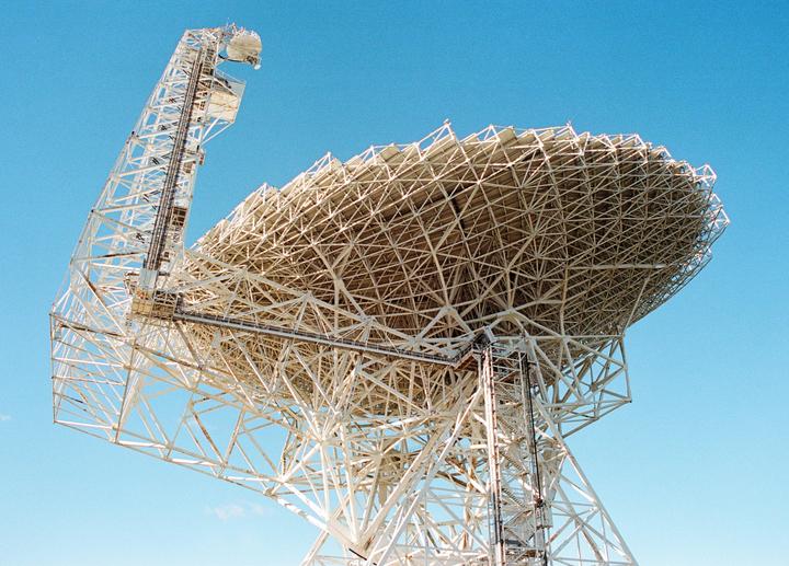 A large white radio telescope dish is angled towards the sky.