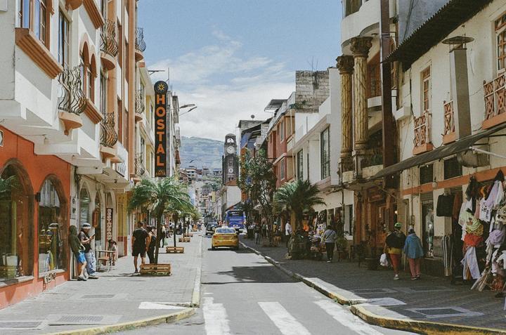 A street with buildings, people, and vehicles is seen under a bright sky.