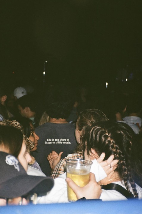 A person wearing a shirt that says "Life is too short to listen to shitty music" is visible in a crowd at night.