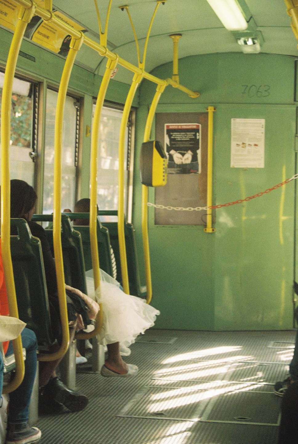 Sunlight streams through the windows of a green bus, illuminating the floor and the white dress of a passenger.