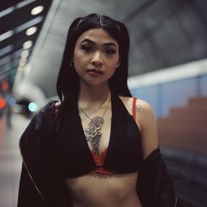 A woman with long dark hair and a black top stands in a subway station.
