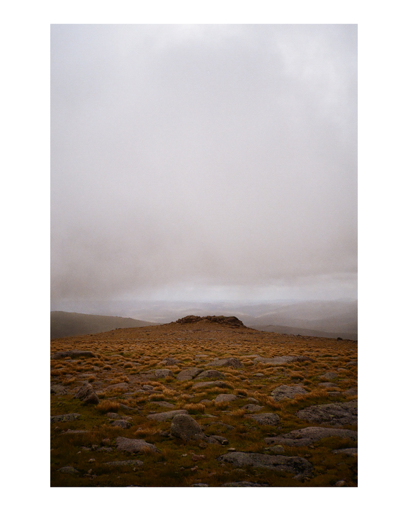 A rocky, grassy hill is visible under a hazy sky.