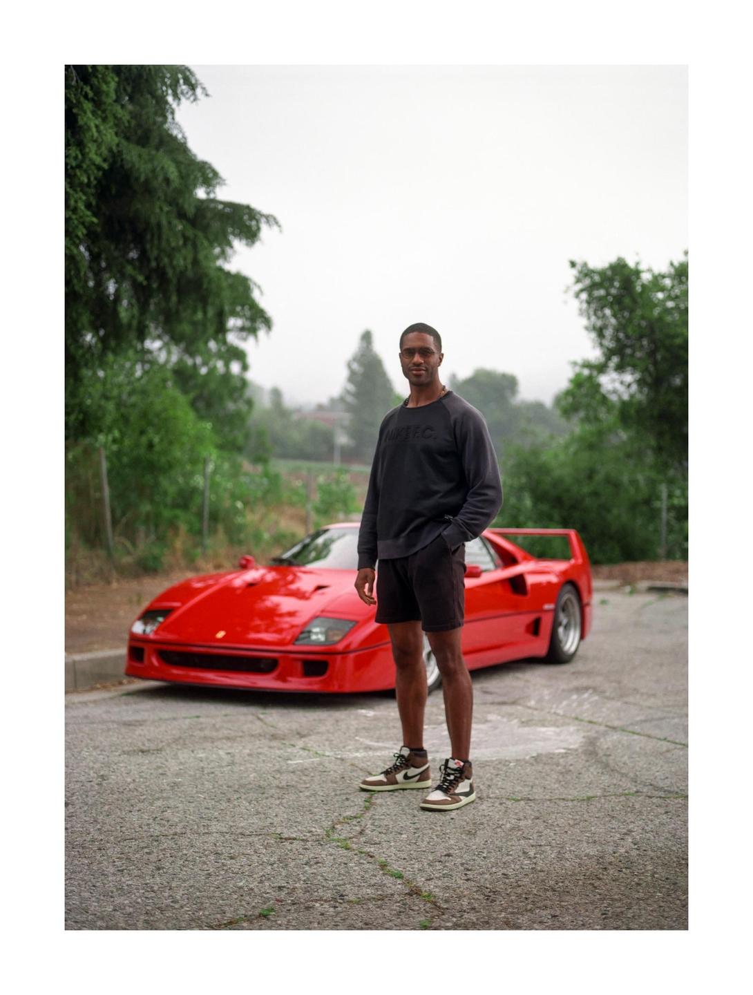 A man stands in front of a red sports car on an overcast day.