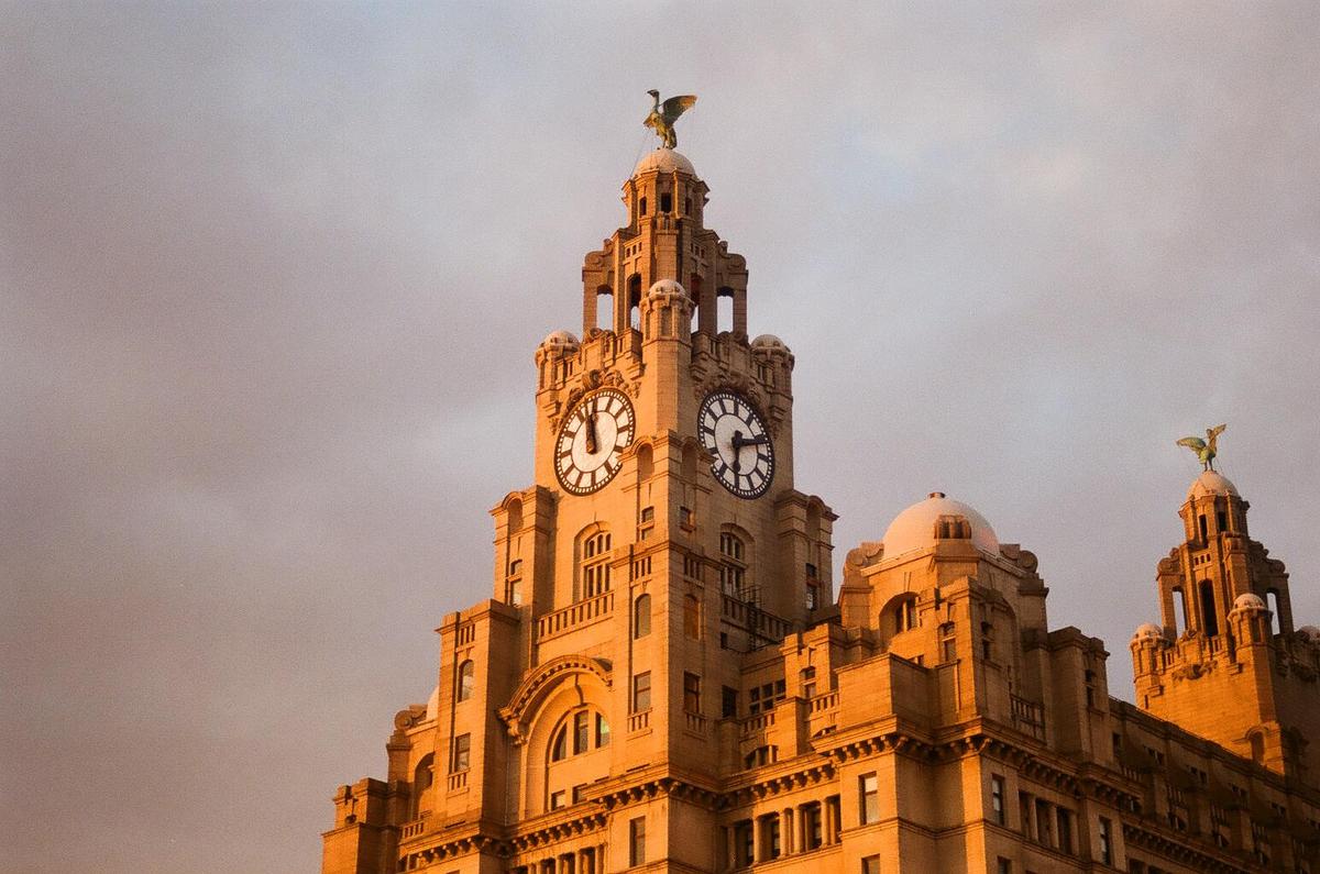 The Royal Liver Building is illuminated by the setting sun against a cloudy sky.