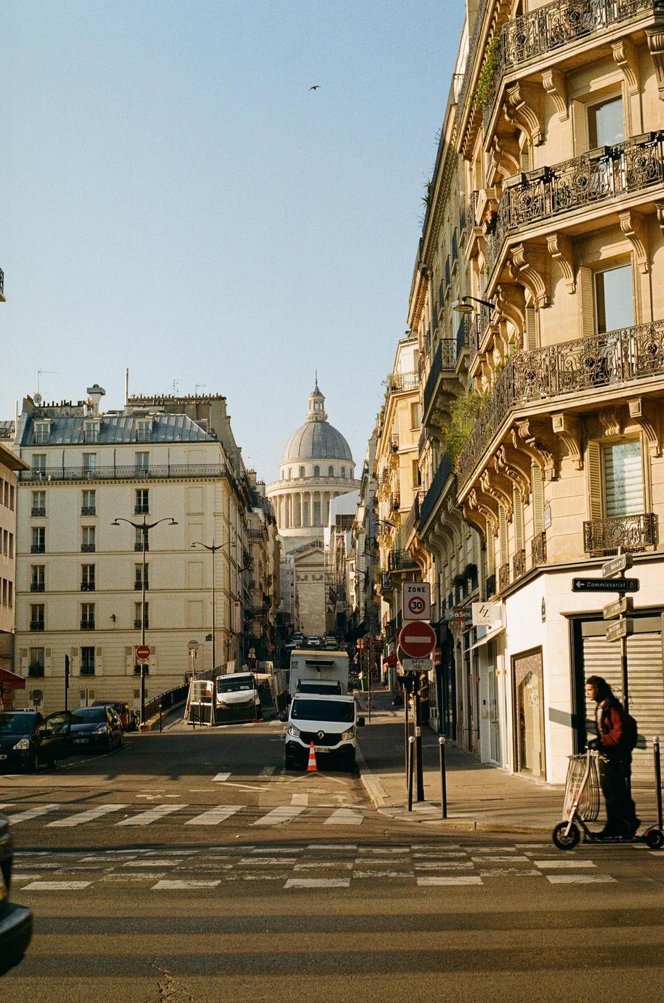 A street in Paris leads to the Pantheon, with a person on a scooter on the right.