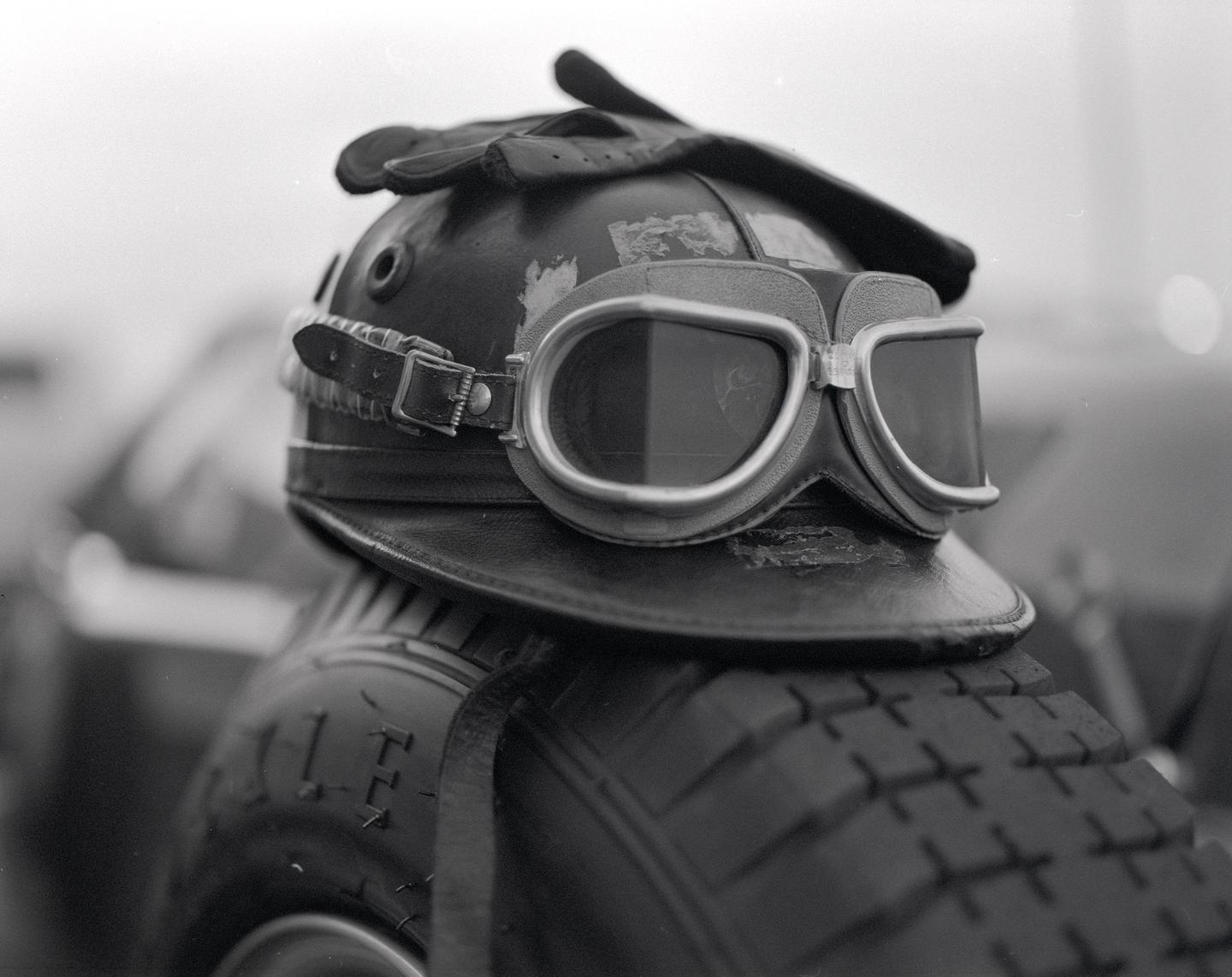 A vintage leather helmet with goggles and gloves rests on a tire.