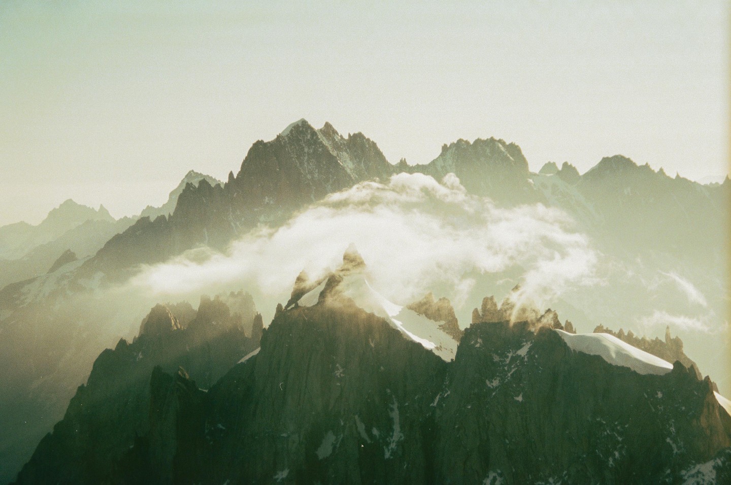 Clouds drift through a range of jagged, snow-capped mountains.