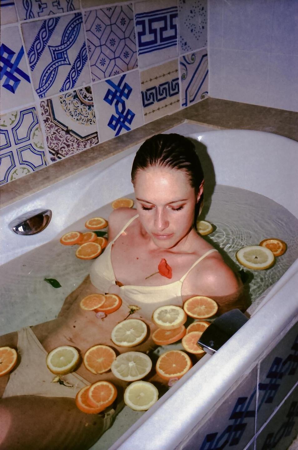 A woman is bathing in a tub filled with water and citrus slices.