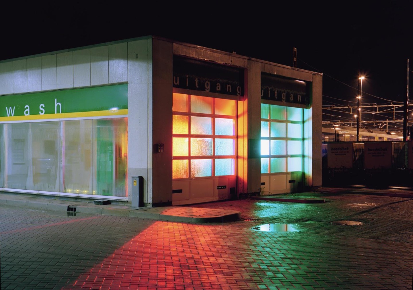 A car wash building with colorful lights reflecting on the wet pavement at night.