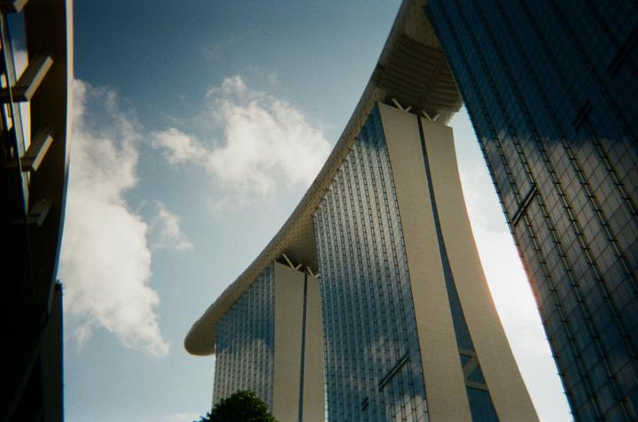 Three modern skyscrapers with a curved roof are visible from a low angle against a cloudy sky.