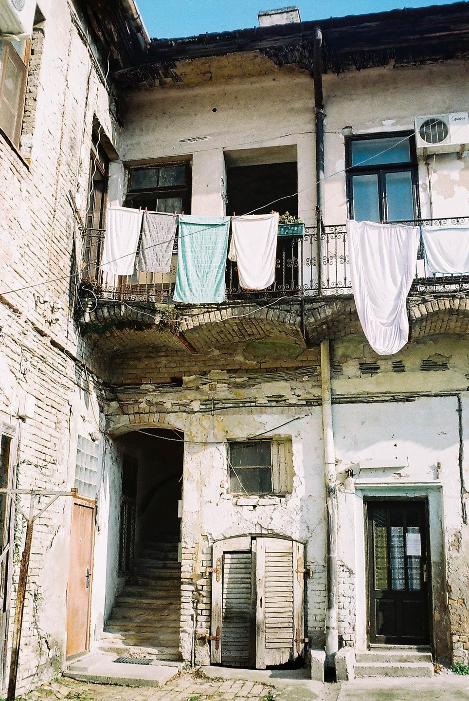 Laundry hangs on a balcony above a courtyard with crumbling walls and multiple doorways.