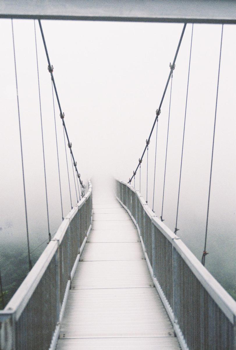 A suspension bridge extends into a thick fog, obscuring its end.