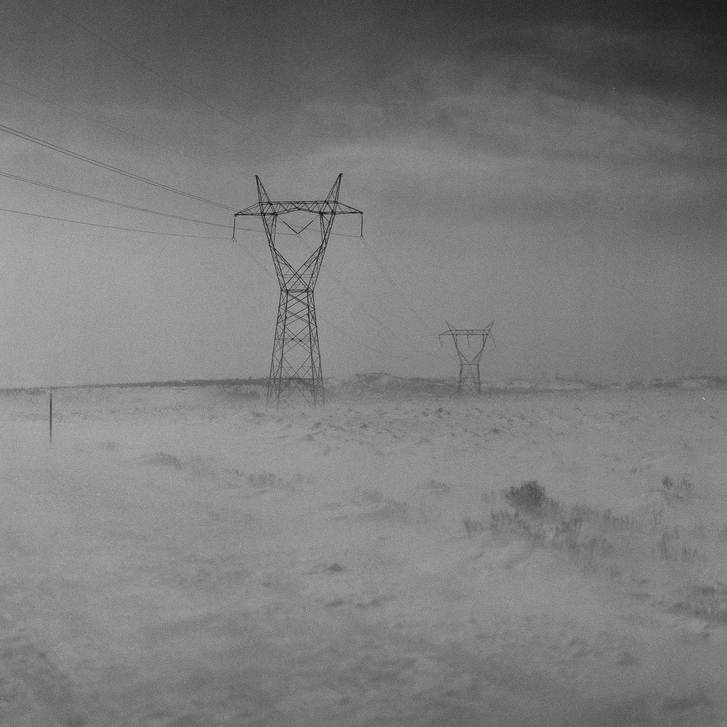 Two electricity pylons stand in a hazy, snow-covered landscape under a dark sky.