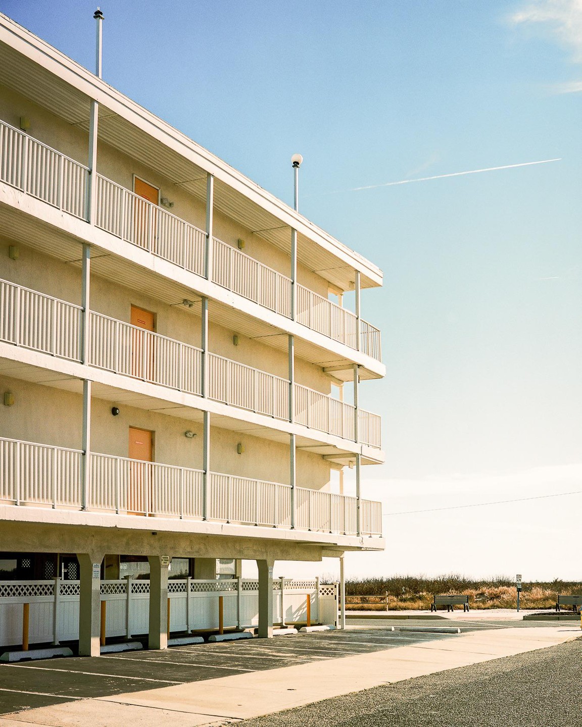 A multi-story motel with balconies and orange doors stands next to a parking lot under a clear sky.