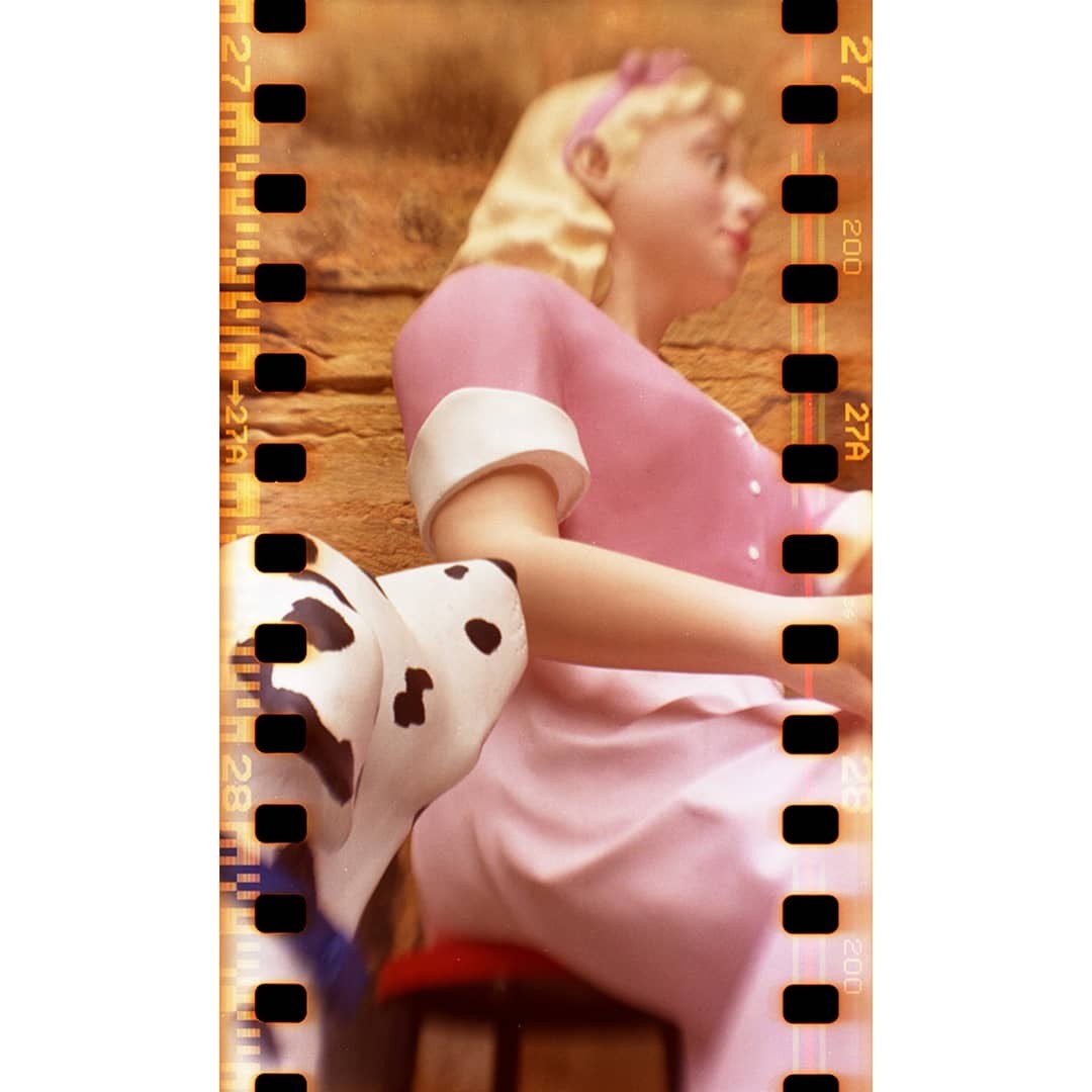 A blonde doll in a pink dress sits next to a dalmatian statue.