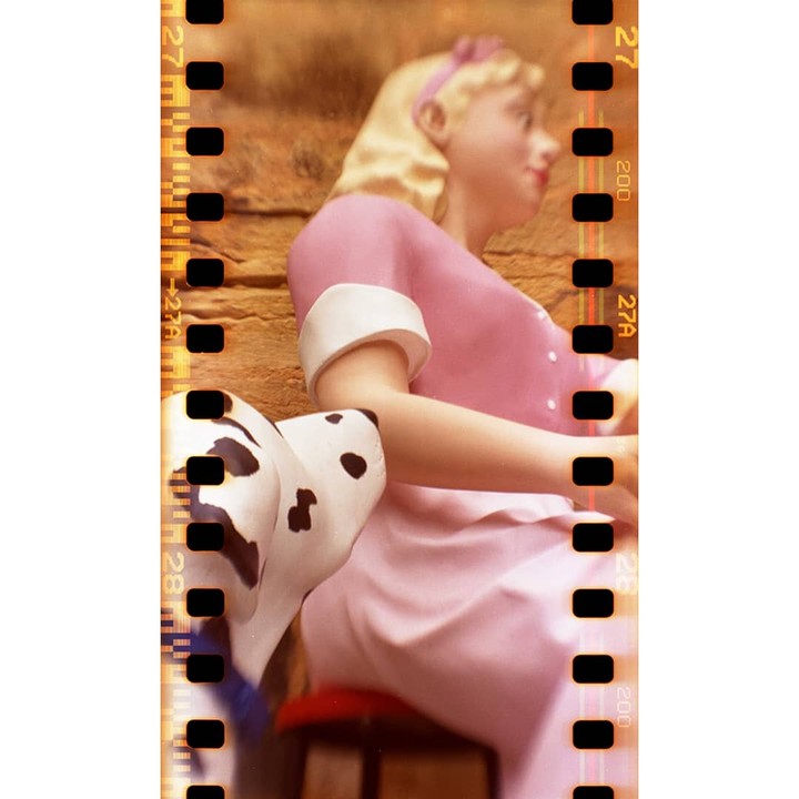 A blonde doll in a pink dress sits next to a dalmatian statue.