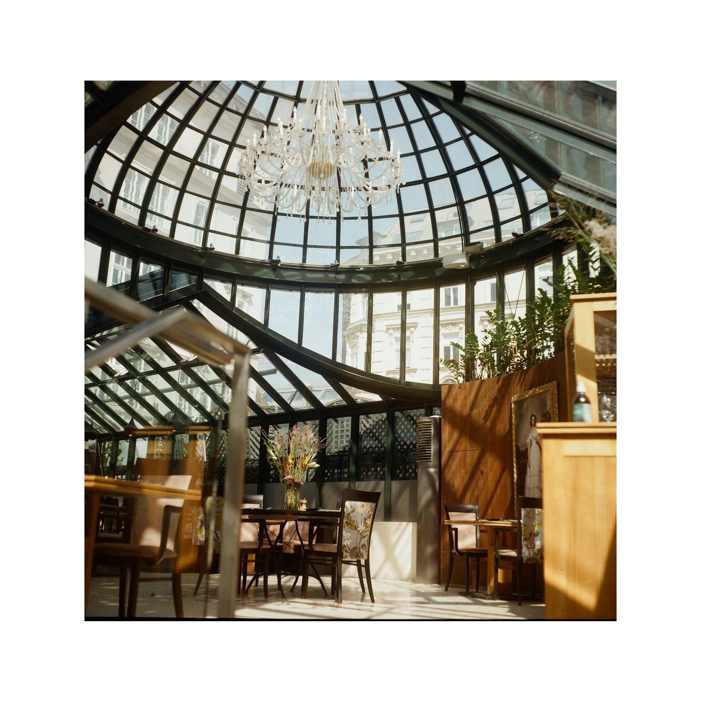 A large glass-domed room with a chandelier and tables is filled with natural light.