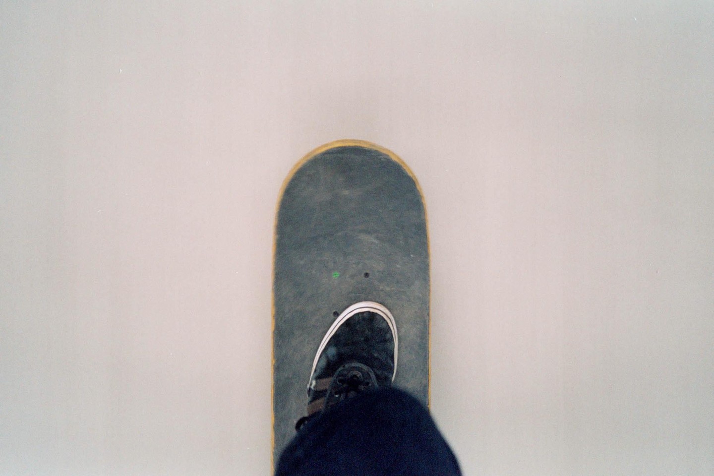A person's foot in a black shoe is on a skateboard.