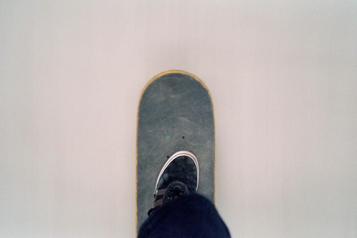 A person's foot in a black shoe is on a skateboard.