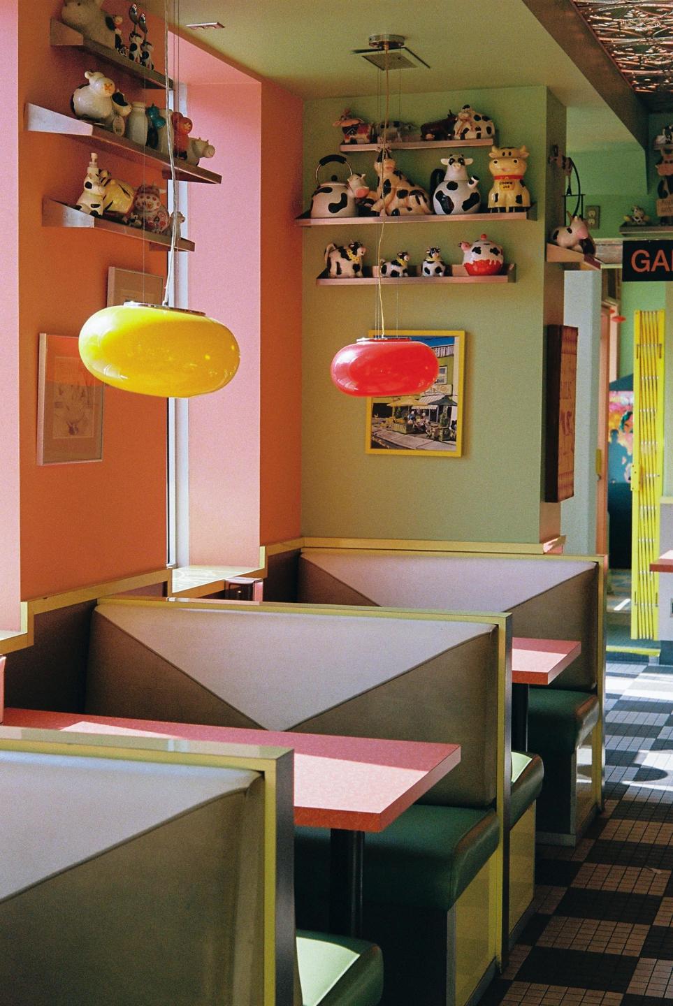 A diner interior features colorful booths, tables, and shelves filled with cow figurines.