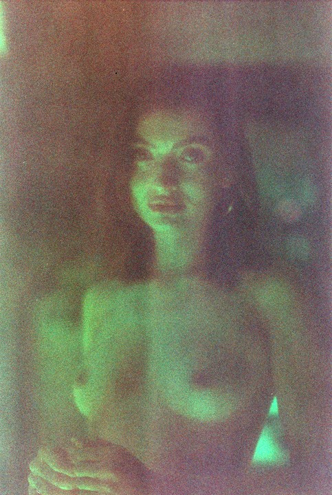 A woman is illuminated by green light in a grainy, dark portrait.