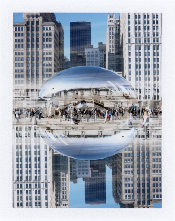 A double exposure shows a reflective bean-shaped sculpture with people and buildings in the background and reflected on its surface.