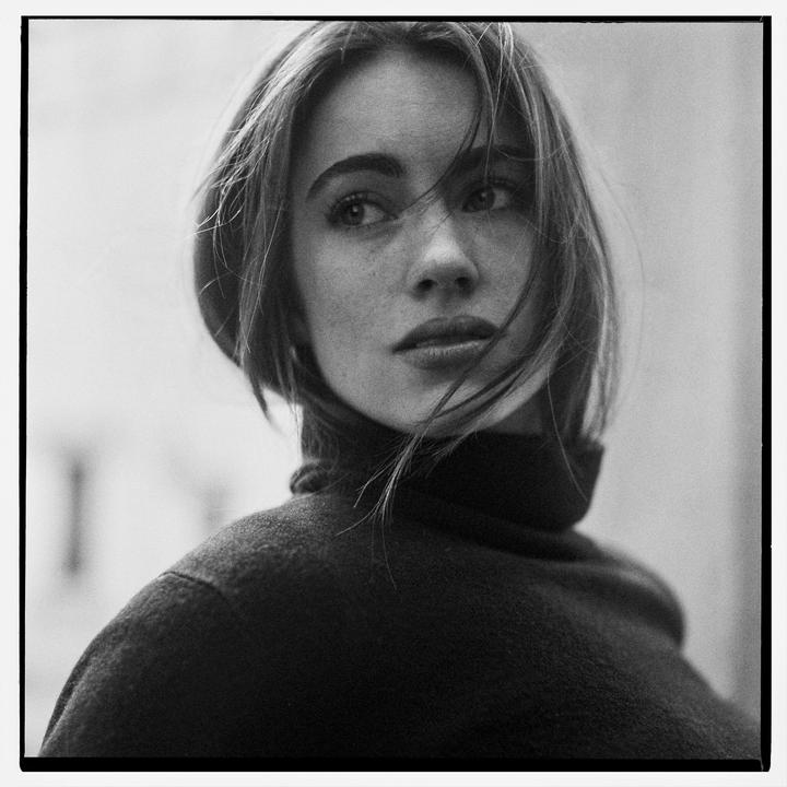 A woman with windblown hair looks to the side while wearing a turtleneck.