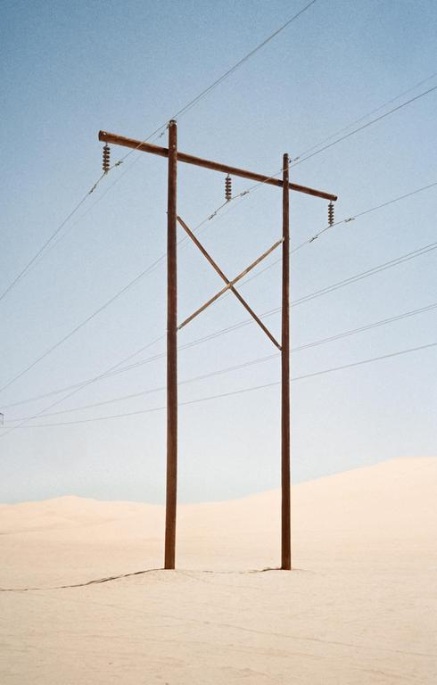 A utility pole with power lines stands in a vast desert landscape under a clear sky.