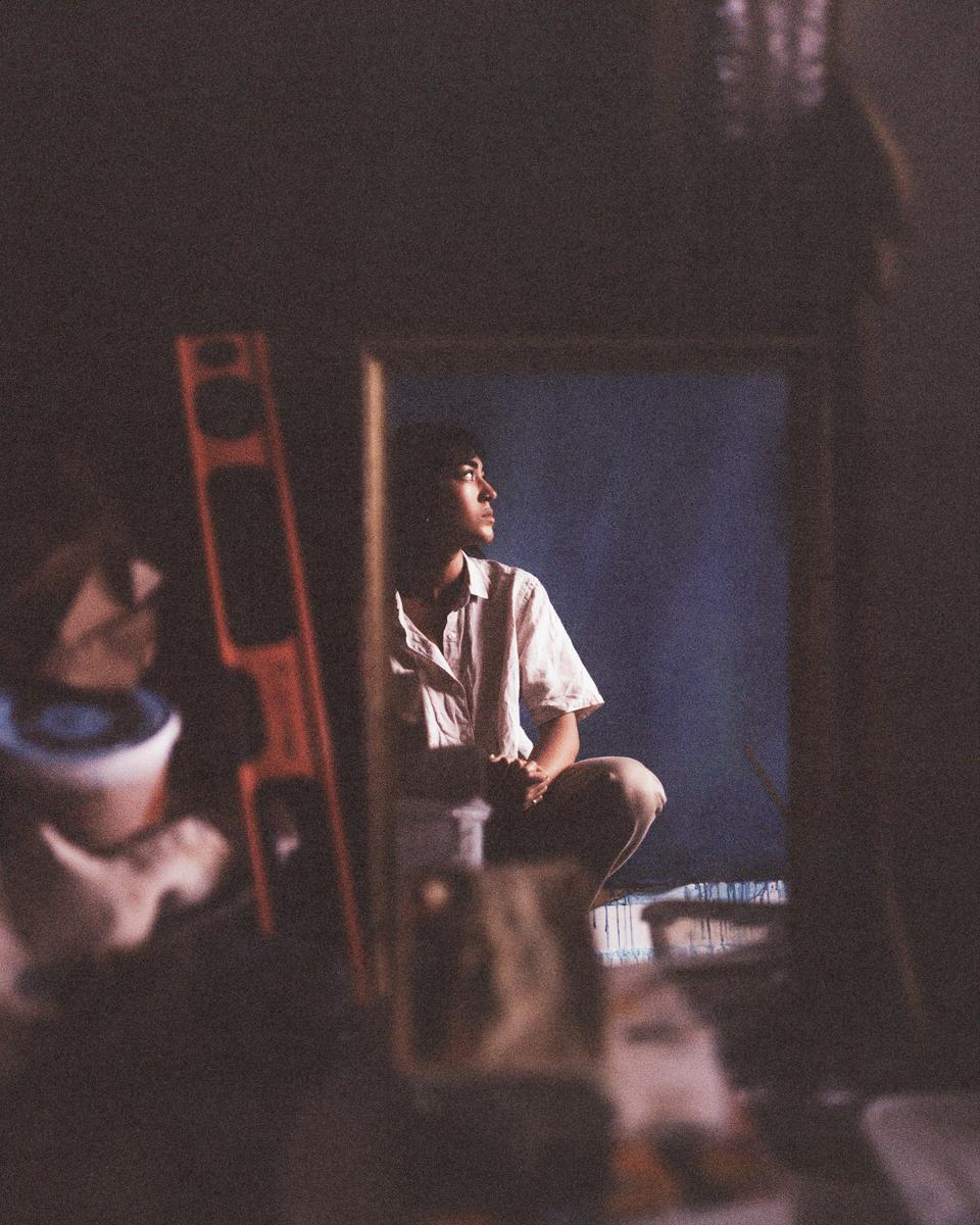 A man crouches in a dimly lit room, looking up and to the right.