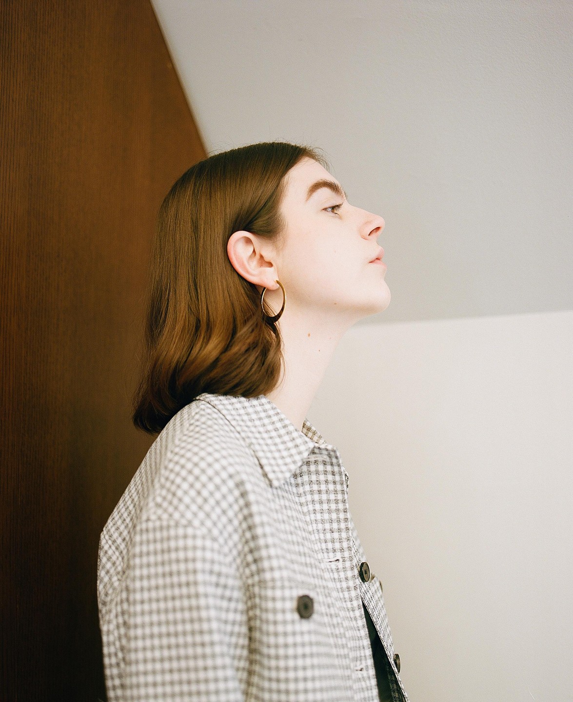 A woman with brown hair and a plaid shirt looks up and to the right.