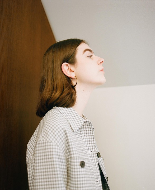 A woman with brown hair and a plaid shirt looks up and to the right.