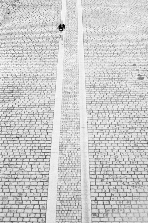 A woman runs on a cobblestone path with two parallel concrete strips.
