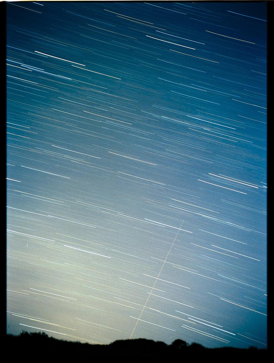 Star trails streak across the night sky above a silhouetted landscape.